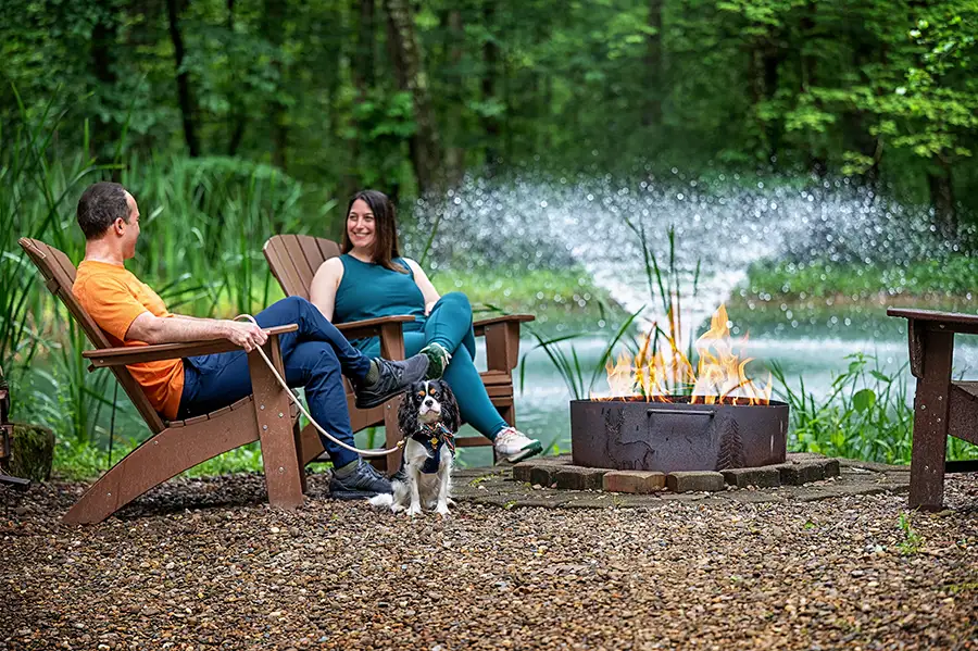 Couple relaxing with their dog beside an outdoor fire pit and private pond at a Hocking Hills cabin