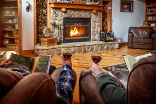 fireplace with fire in background, couple in chairs with glasses of wine, reading books