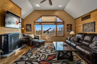 Living room with leather couch on the side. Large window with telescope on far wall, TV and fireplace on the left wall. 