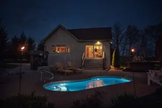 Cabin exterior at night. Private pool glowing blue in the dark. Warm lights glow in the cabin. 