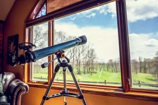 Telescope facing out the large living room windows, rolling hills and sky views in the background. 