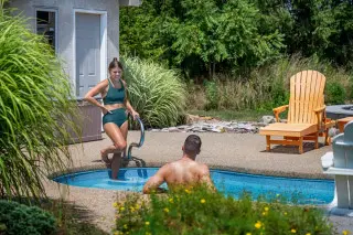 Woman on the steps to a swimming pool, man resting in the pool