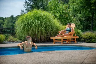 A man relaxes in a pool, woman sunbathing in a chair nearby