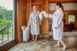 Man and woman standing in robes, grabbing a towel from the towel warmer