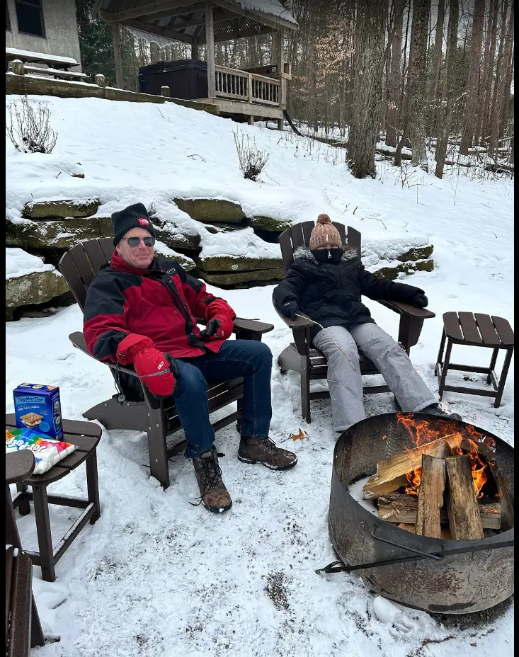 Man and woman sit around a campfire, snow surrounding