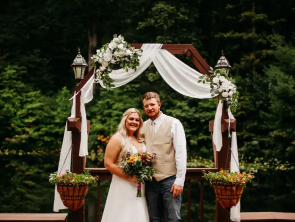 Bride and groom stand in front of the decorated archway.