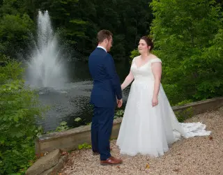 Bride and Groom stand facing one another in front of the lake fountain