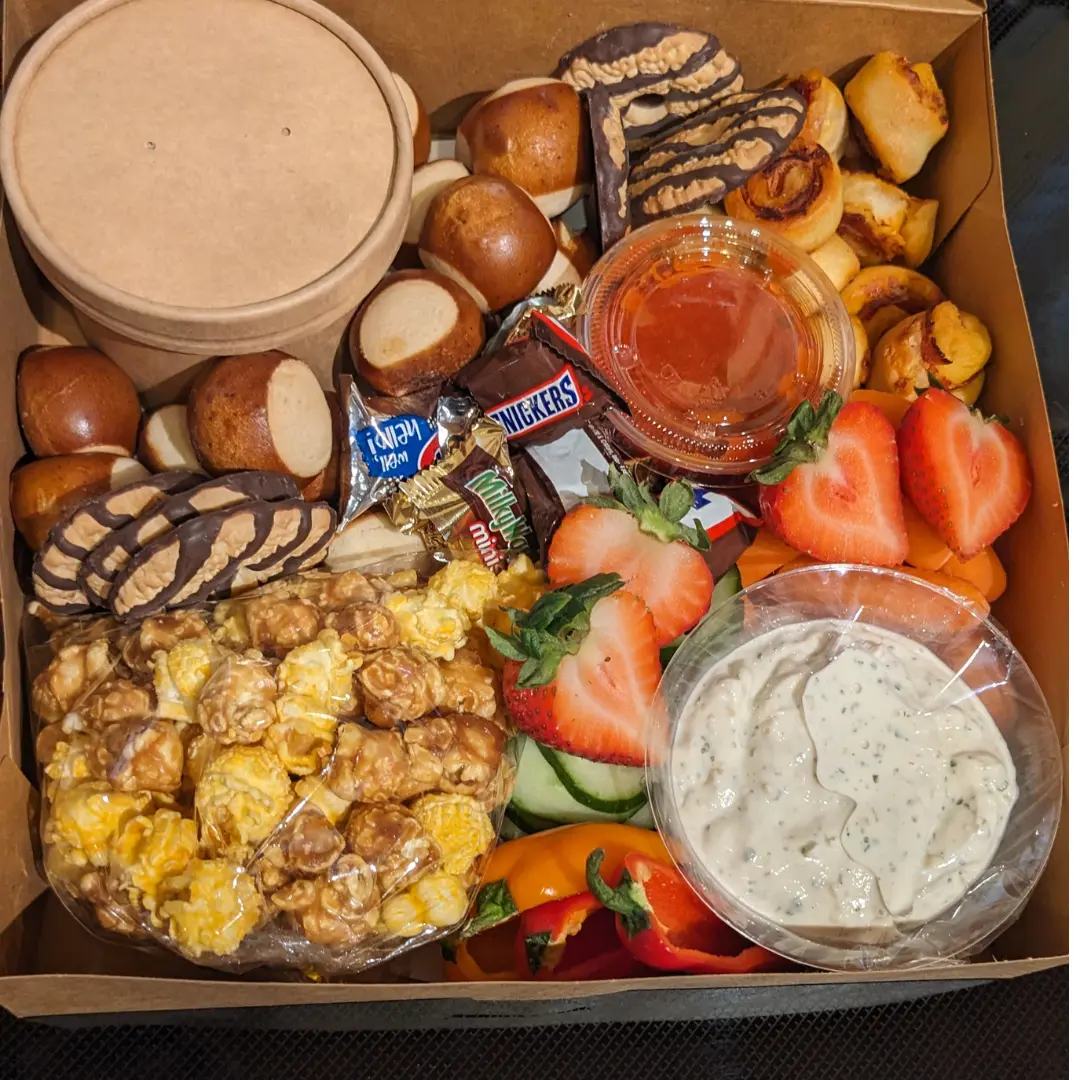 photo of a box with snacks. Caramel corn, pretzel bites, pepperoni roll bites, strawberries, mini candies and more.