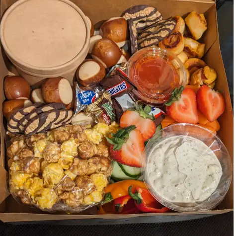 photo of a box with snacks. Caramel corn, pretzel bites, pepperoni roll bites, strawberries, mini candies and more. 