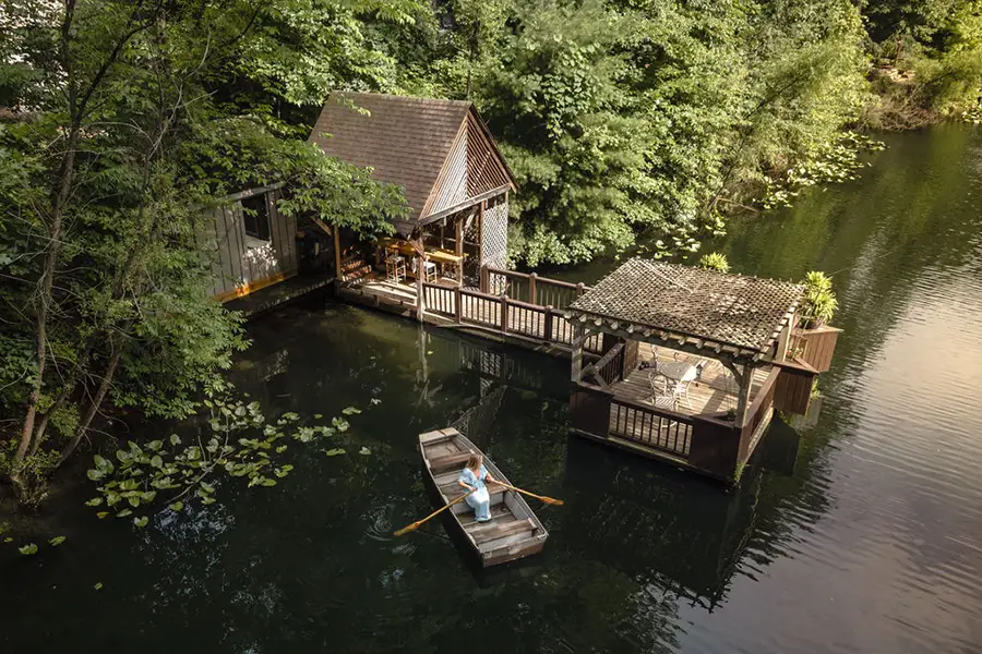 Wooden boathouse and dock surrounded by trees with a small rowboat on the lake.