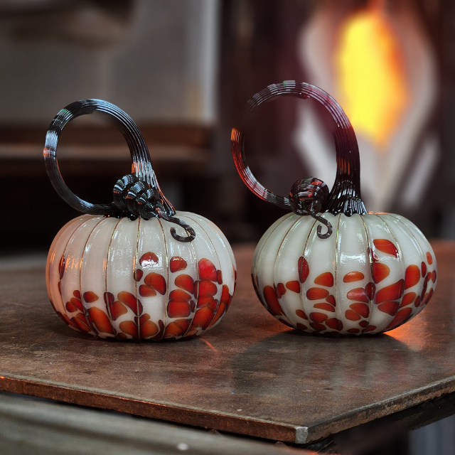 Two white and orange glass blown pumpkins sitting on a counter