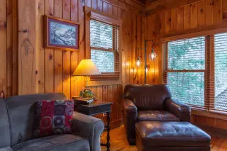 Leather armchair and couch in living room, wooden cabin walls in background