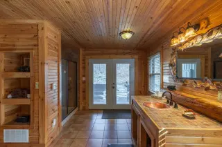 Bathroom with heated floors, copper sink and mirror on the right, shower on the left. Doors to hot tubs in background. 