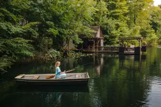 Woman sits in a row boat on the lake, scenic dock in the background