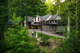 A man and woman walk down a stone pathway, lodge in the background, greenery surrounding