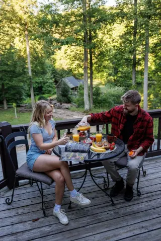 A man and woman enjoy a brunch meal at an outdoor table, lakeside gazebo in the background