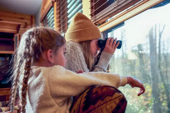Two children looking out a window, one with binoculars