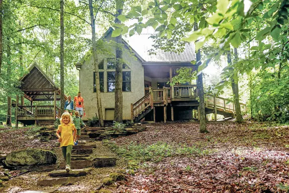 Cabin with stone walkway, woods surrounding. A child runs down the steps.