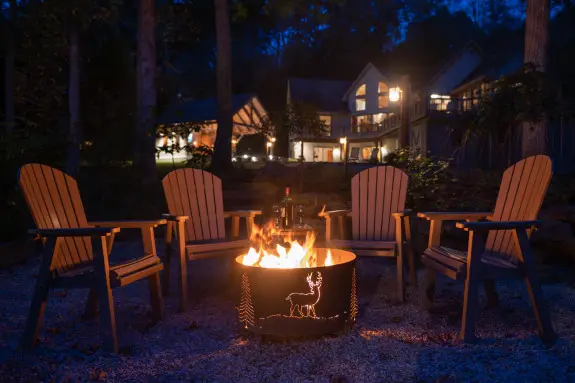 Night shot, a fire burning in custom fire pit, chairs surround. A cabin glowing in the background. 