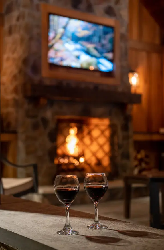 2 wine glasses sitting in front of fireplace with fire burning