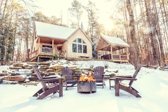 Still waters cabin situated in secluded woods, stone steps lead up to cabin. Snow dusting covers cabin and grounds