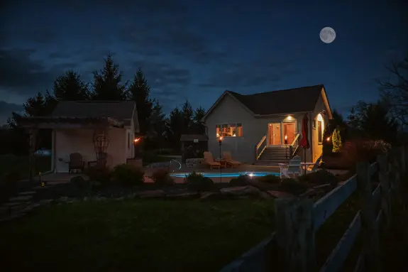 Cabin exterior at night. Private pool glowing blue in the dark. Warm lights glow in the cabin. 