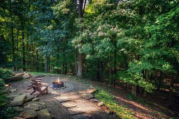 Stone pathway leading to two adirondack chairs and a fire burning in a custom fire ring