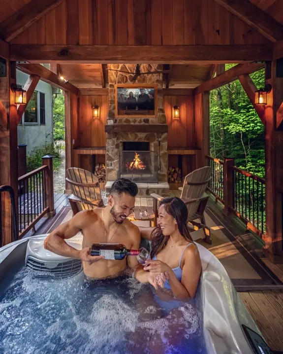Couple enjoying wine in the bubbling hot tub, with fireplace and tv in background