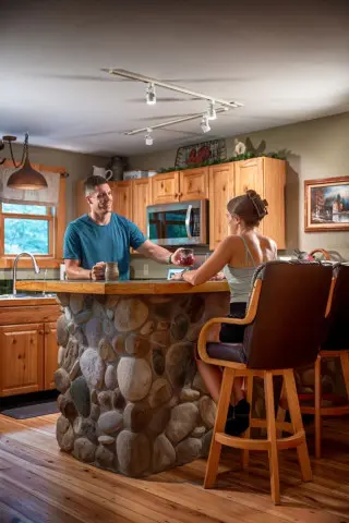 Man stands at the kitchen bar. Woman sits in bar chair, drinking coffee