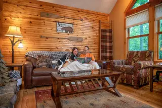 Man and woman relaxing under a throw blanket on a couch, dog is there too. 