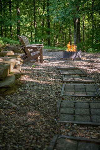 Stone pathway leading to two adirondack chairs and a fire burning in a custom fire ring