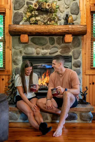 A man and woman hit in front of a fireplace, with mugs. 