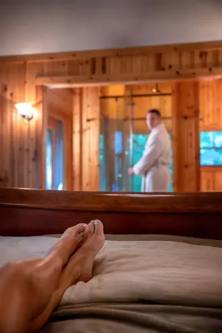 A woman's legs in focus on a bed, a man in a robe in the background