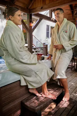 Man and woman stand by a hot tub in robes