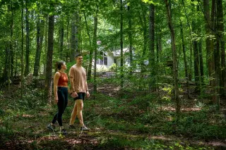 A woman and man walking in the forest, cabin in the background