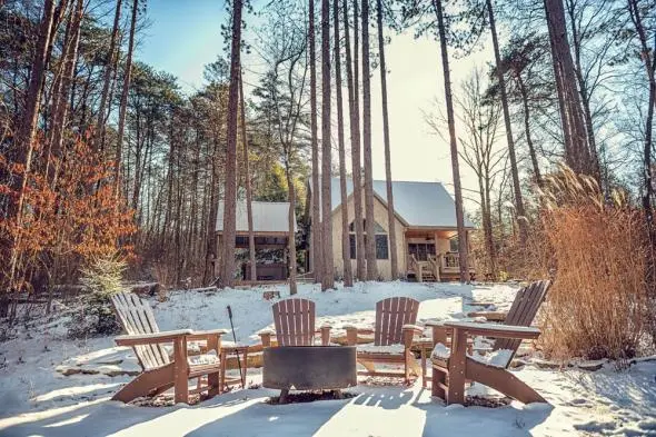 fire ring and adirondak chairs surrounding, cabin in the background, everything coated in snow