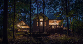 Cabin glows with warm light at night, nestled in the woods